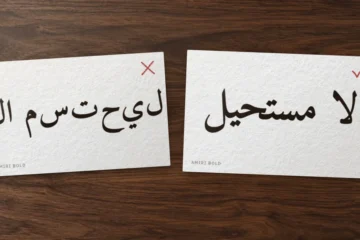 Two cards on a desk: لا مستحيل in Amiri as isolated letters set left to right, crossed out, and correctly joined, ticked