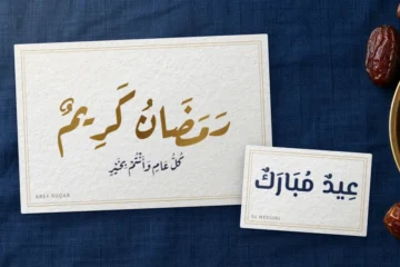 Greeting cards on navy linen: “Ramadan Kareem” in gold Aref Ruqaa and “Eid Mubarak” in El Messiri, beside a brass plate of dates
