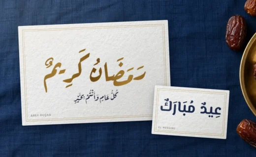 Greeting cards on navy linen: “Ramadan Kareem” in gold Aref Ruqaa and “Eid Mubarak” in El Messiri, beside a brass plate of dates
